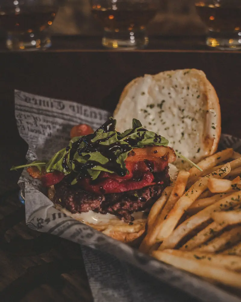 A burger stacked with bacon, arugula and balsamic glaze, with fries