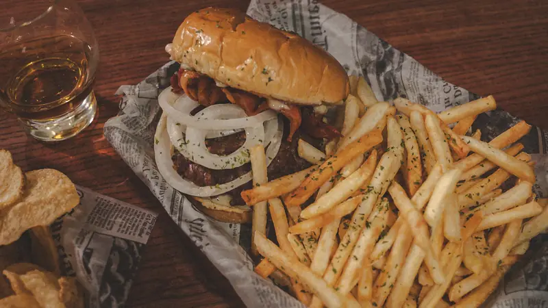 A burger with sweet onion and bacon next to a pile of fries