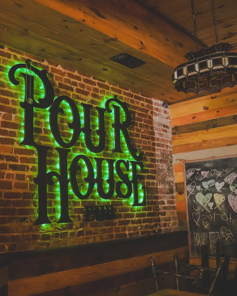 The green-lit Pour House sign on the brick wall