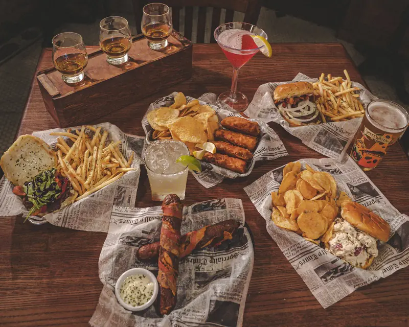 A table crowded with burgers, fish and chips, pretzels and a whiskey flight